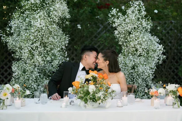 Bride and groom kissing at a flower-decorated wedding reception table