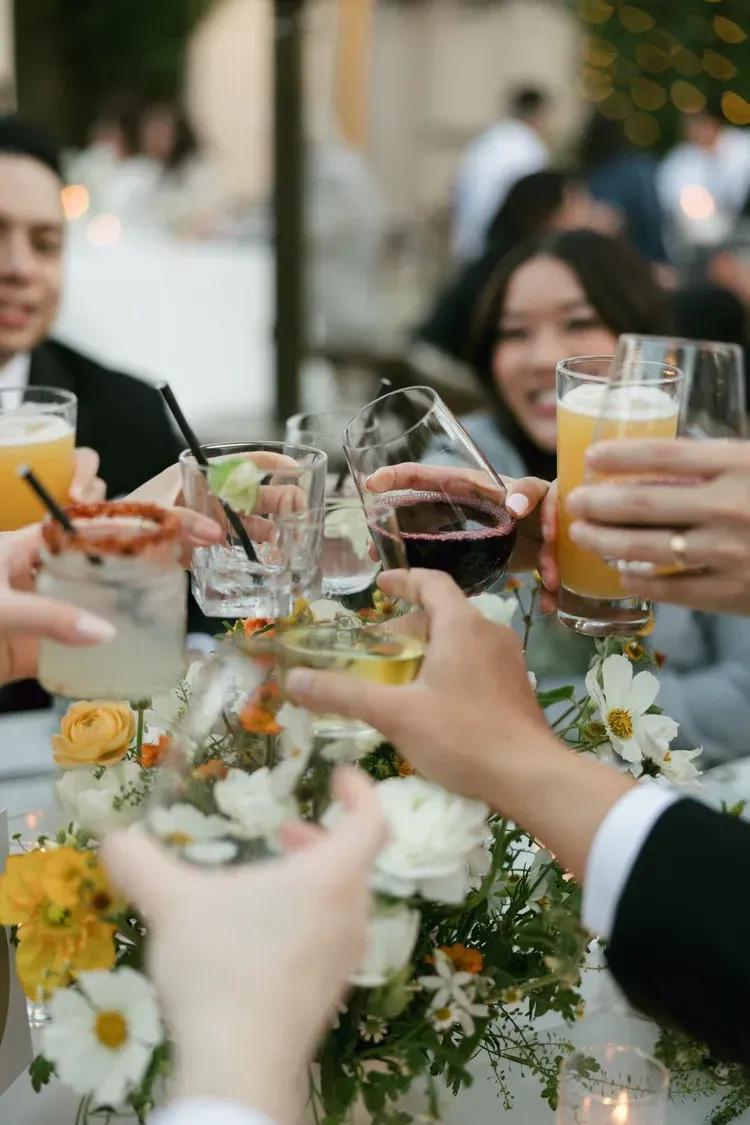 Friends toasting with champagne and cocktails around a flower-filled table at a lively celebration