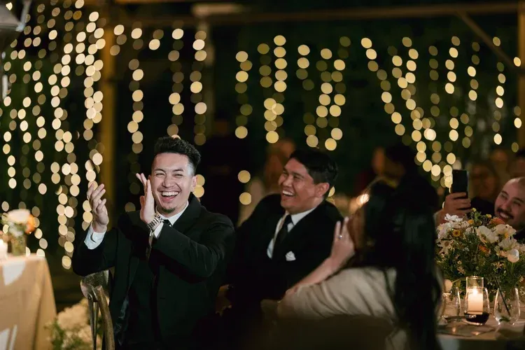 Guests clapping at a warmly lit evening celebration with string lights and candles.