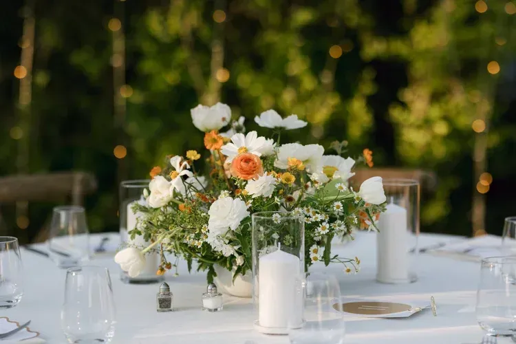 Elegant outdoor table centerpiece with white and peach flowers, candles, and glassware at a wedding reception