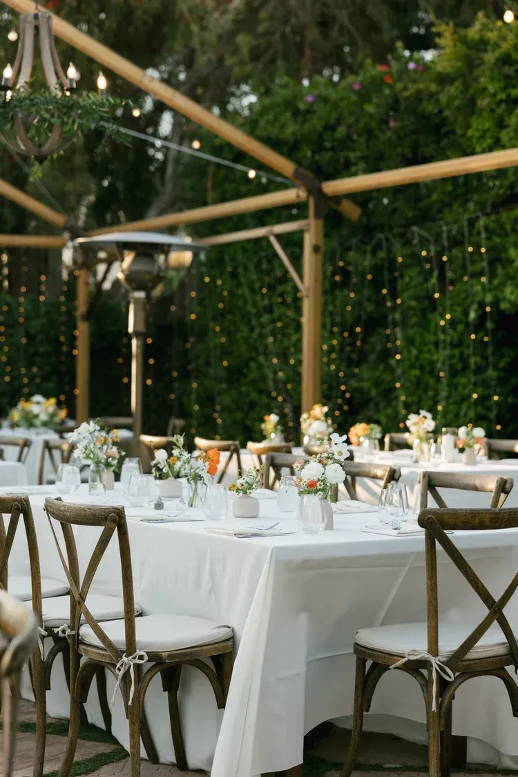 Outdoor wedding reception tables set with white linens and floral centerpieces under a wooden pergola.