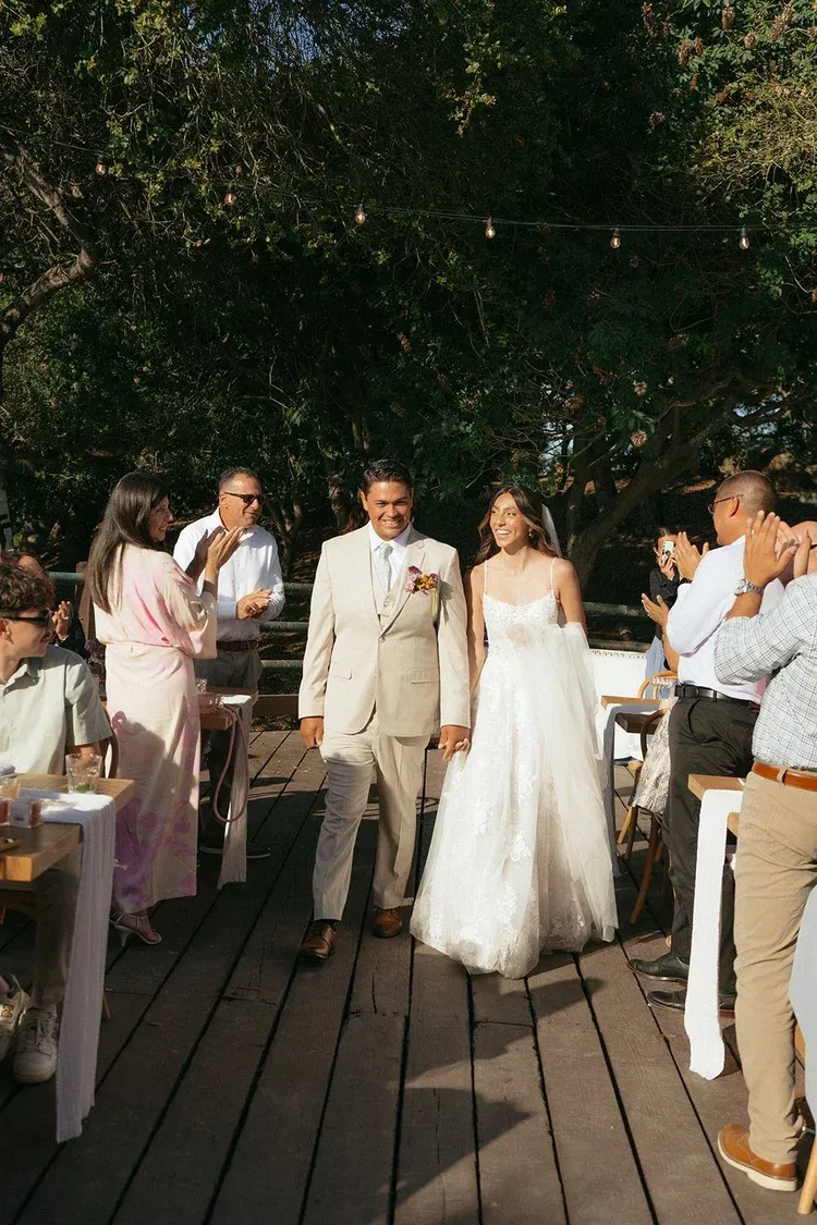 Wedding couple walking down outdoor wooden aisle with guests applauding in the background