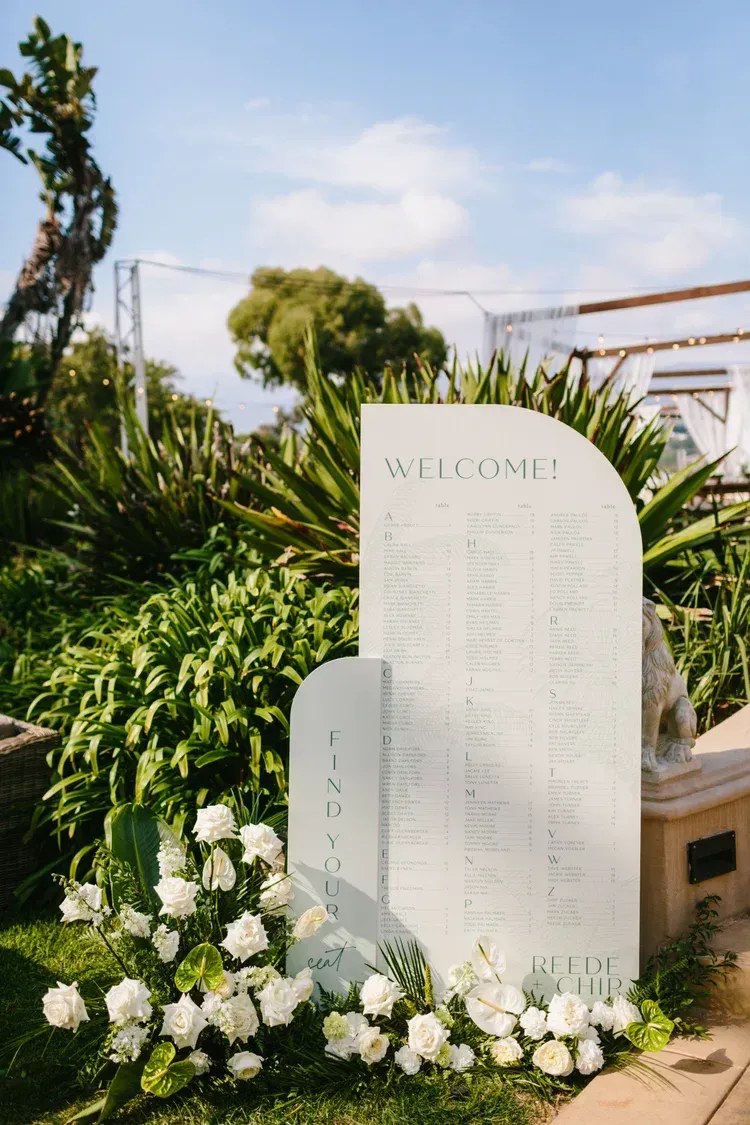 White memorial stone among lush greenery and white flowers outdoors under a blue sky