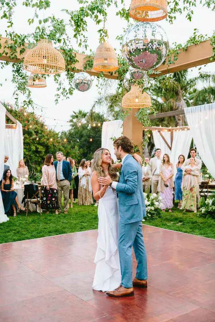 Bride and groom dancing on a decorated outdoor reception floor under hanging florals