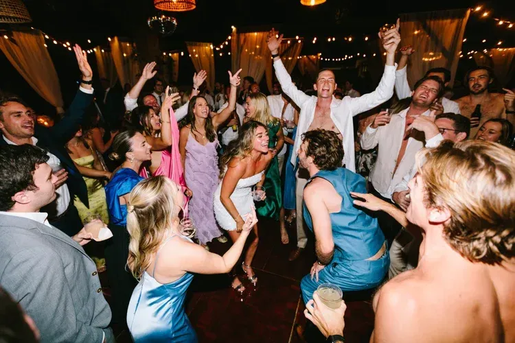 Crowd dancing and cheering at a lively indoor party with warm lights and raised arms