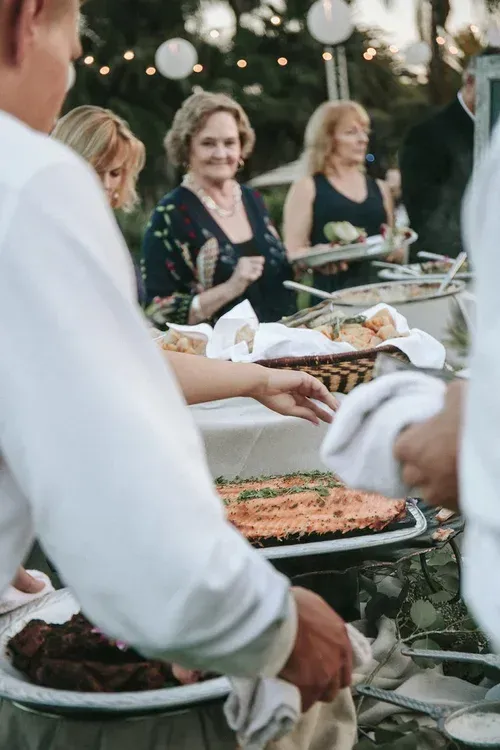 People serving a buffet at an outdoor gathering with string lights