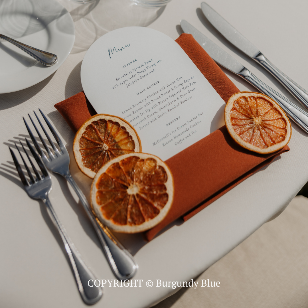 Elegant table setting with orange slices, white menu card, and silverware on a white plate