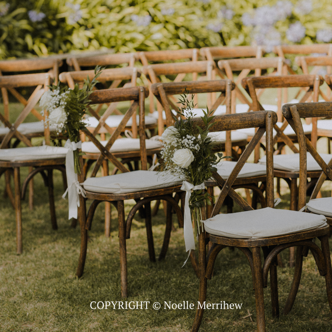 Rustic outdoor wedding chairs with white cushions and greenery on a grassy lawn