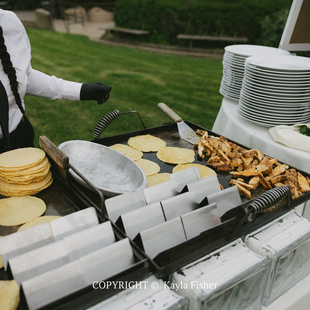 Outdoor buffet with tortillas, grilled chicken, and plates being served at a backyard event