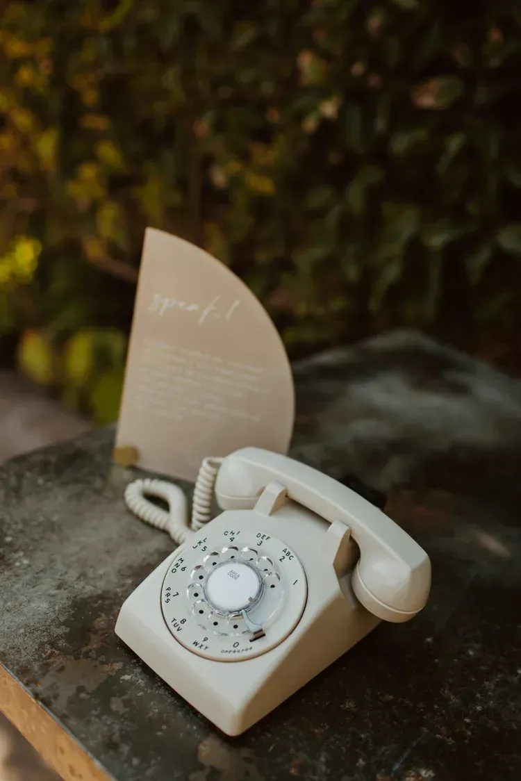 Cream rotary telephone on a table with a handwritten card behind it.