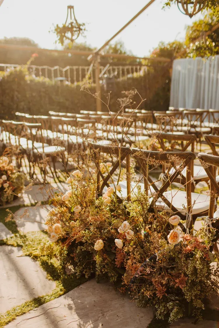Outdoor wedding ceremony setup with rows of gold chairs and floral arrangements in warm sunlight