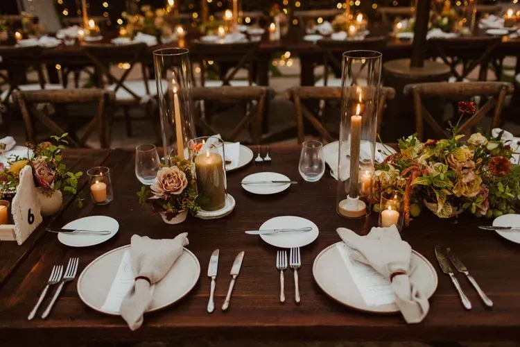Elegant candlelit dinner table set with white napkins, floral centerpieces, glassware, and warm ambient lighting