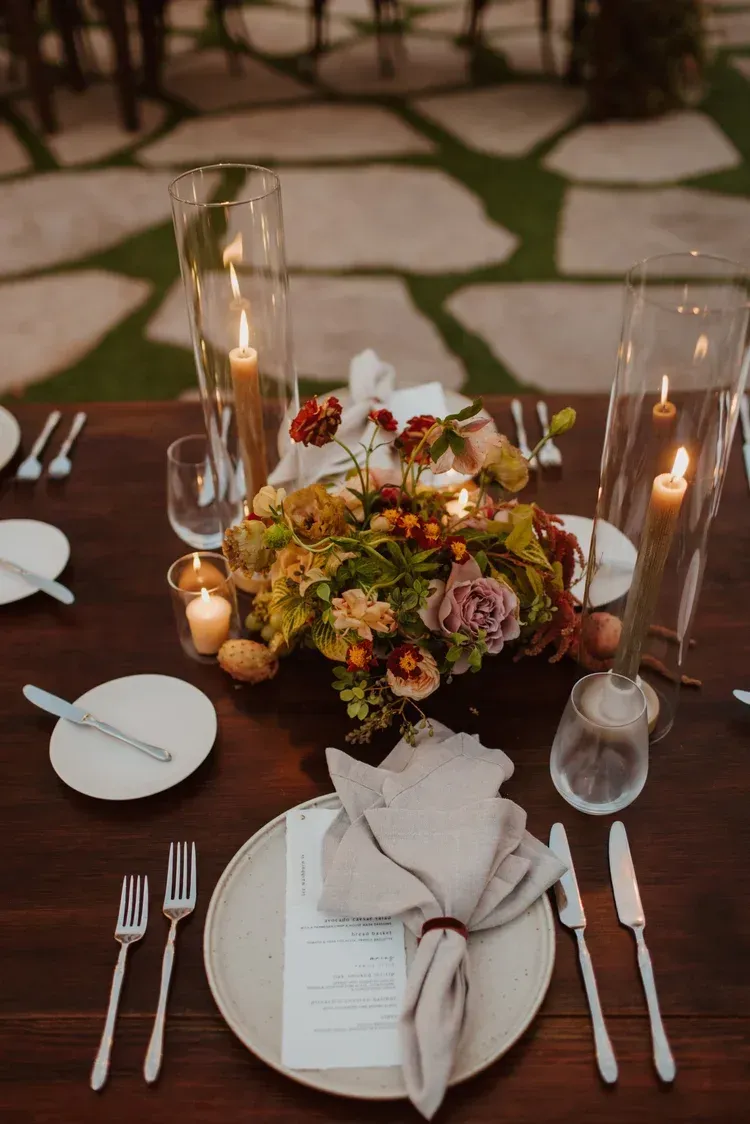 Elegant candlelit table setting with floral centerpiece, white plates, and folded napkins outdoors at dusk
