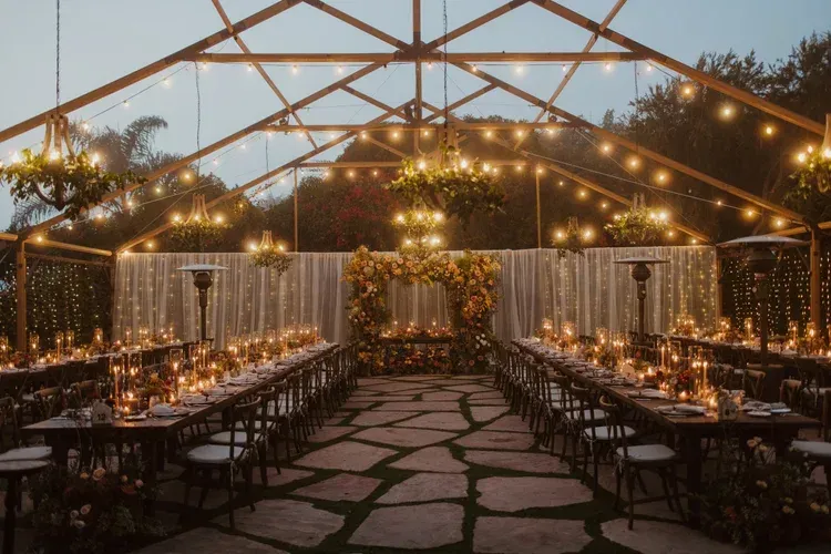 String-lit outdoor dining tent with long tables, stone path, and warm evening ambiance