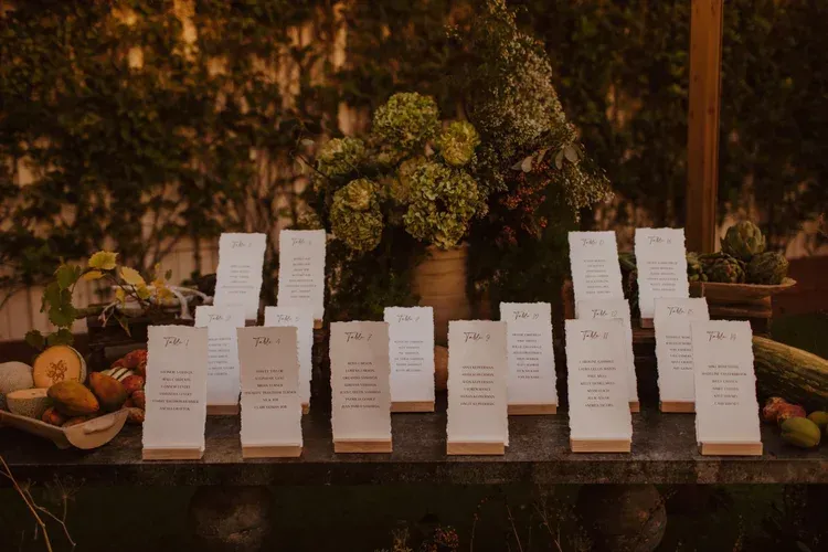 Rows of white place cards on a table with warm floral decor in the background