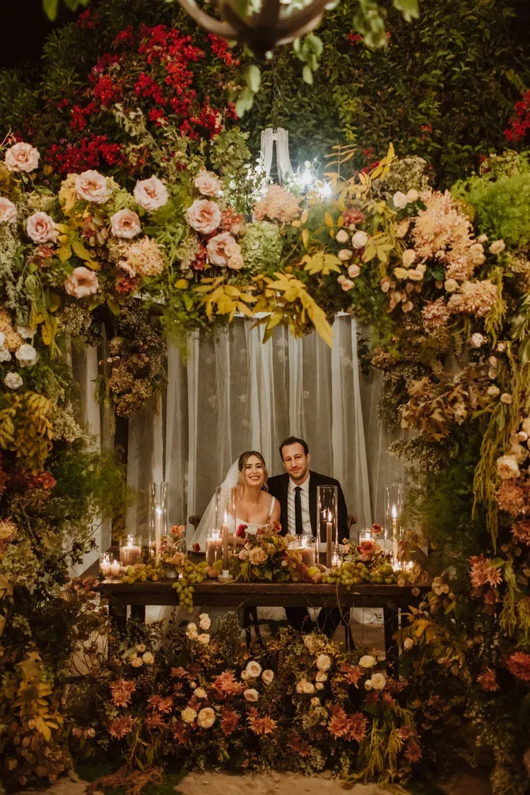 Couple seated at a floral wedding altar with candles and cascading white drapery