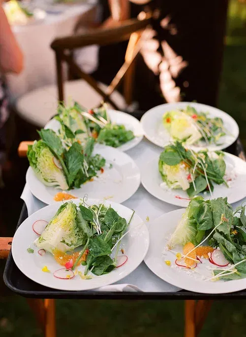 Plates of fresh green salad topped with herbs and orange garnish on a table outdoors