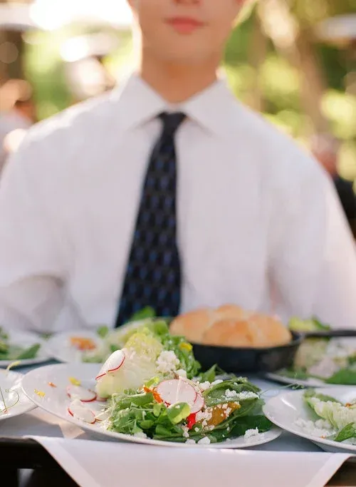 Person in white shirt and tie seated at a table with a salad and bread in the foreground