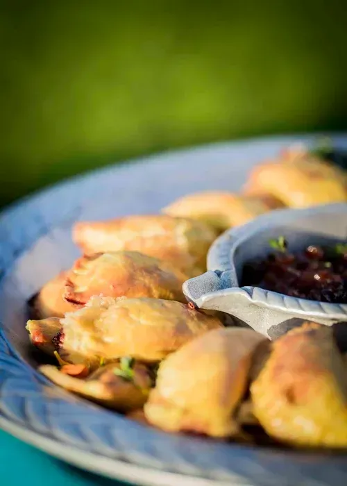 Plate of golden baked pastries with a bowl of dark dipping sauce on a blue tray