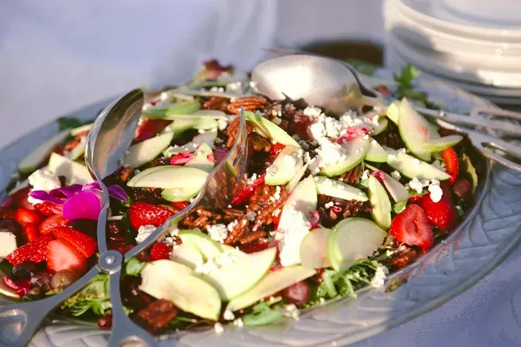Salad with sliced vegetables, strawberries, and herbs in a glass bowl on a table