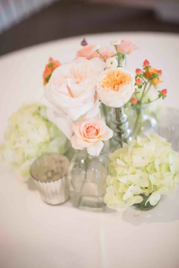 Pastel floral table centerpiece with white and peach roses in glass vases and votive candles