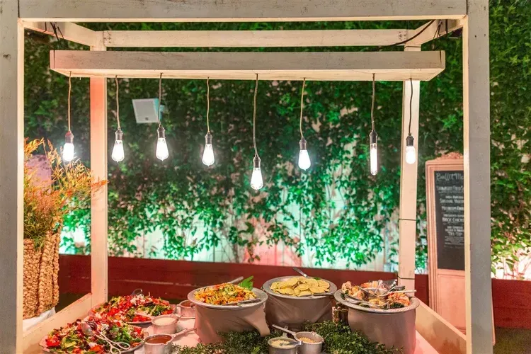 Buffet counter under hanging lights with bowls of food and green vine backdrop