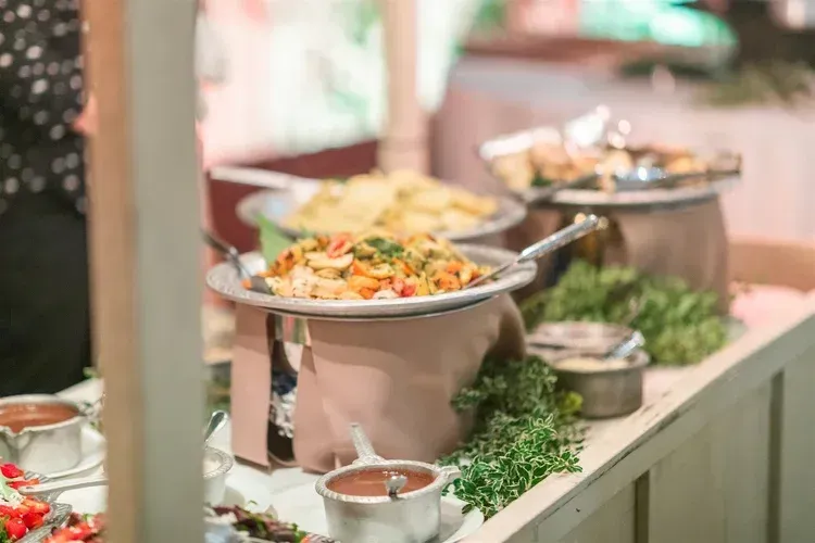 Buffet table with covered dishes, salad bowls, and fresh herbs at a catering setup