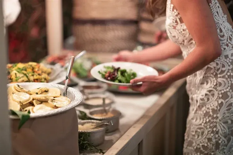 Woman in a lace dress serving salad at a buffet table with appetizers and dishes