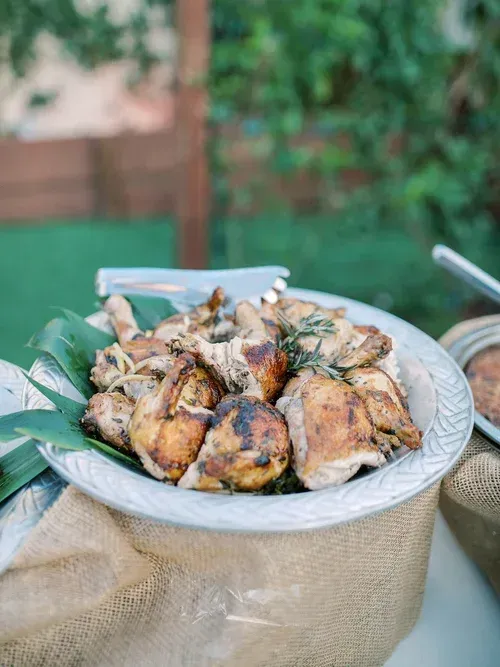 Tray of roasted chicken pieces garnished with herbs on a table outdoors