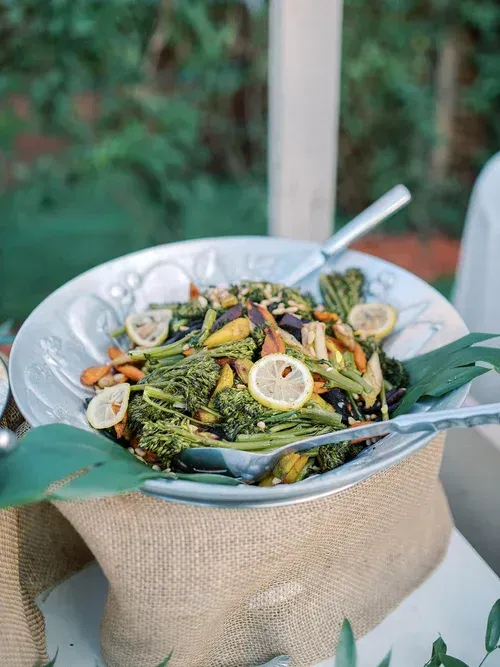 A bowl of salad with lemon slices and tongs on a table outdoors, wrapped in burlap.