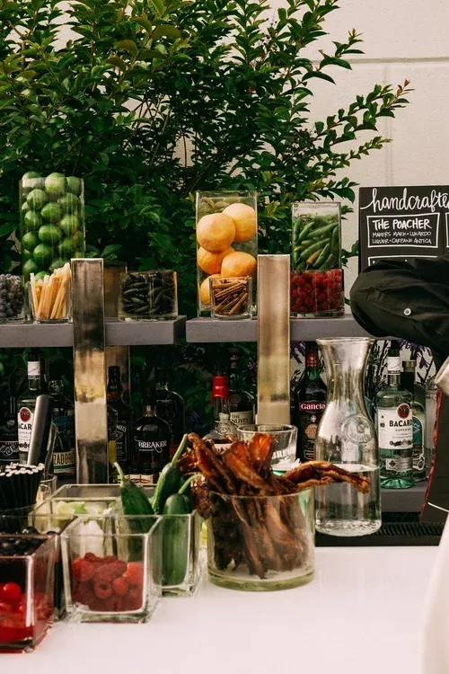 Jars of green apples and dried fruit on a market stall with a handwritten sign and potted greenery