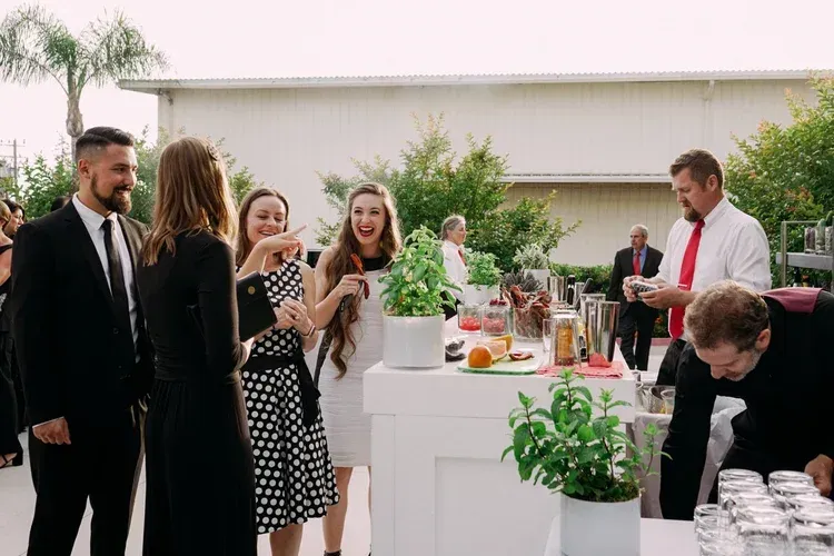 Guests socializing at an outdoor cocktail reception by a white buffet table