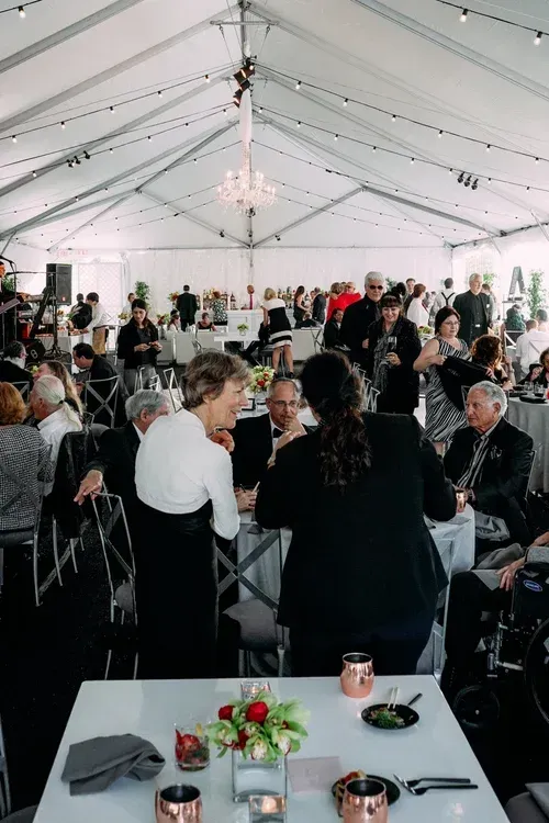Guests seated and mingling under a white event tent at a formal reception