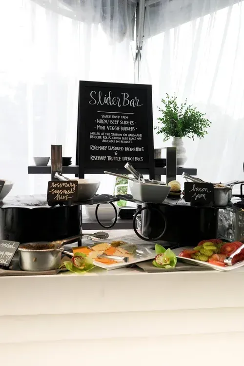 Buffet table with salad bar, black sign, and trays of fresh food in a bright windowed room