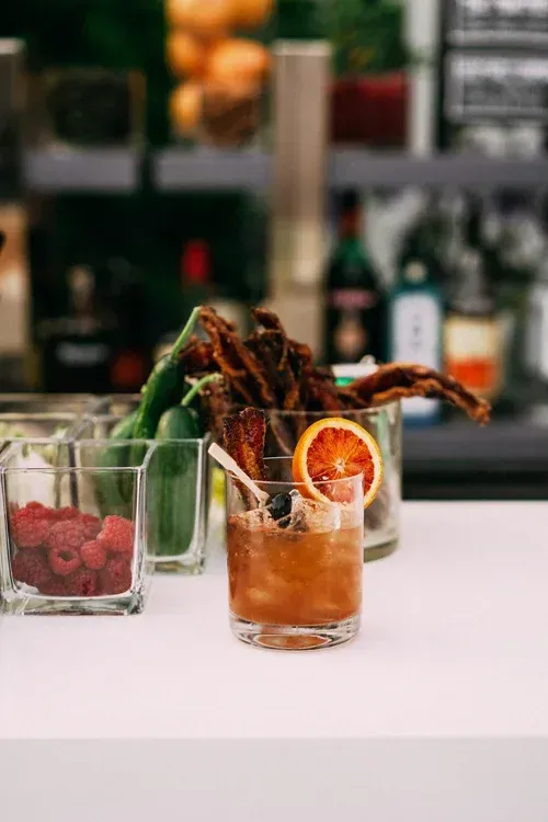 Three colorful cocktails on a bar counter, one garnished with an orange slice and chocolate sticks