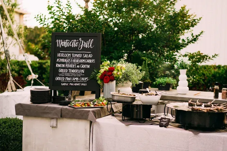 Buffet dessert table with chalkboard menu, fruit garnish, and serving dishes outdoors