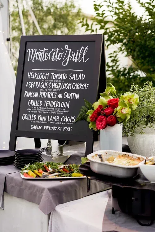 Buffet table with chalkboard menu, salad, roast potatoes, gratin and flowers in a catered event setting