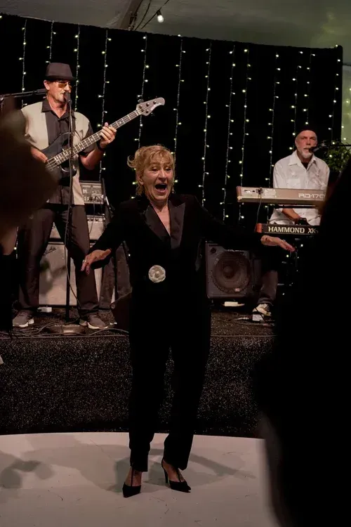 Singer performing onstage in front of a live band with string lights in the background