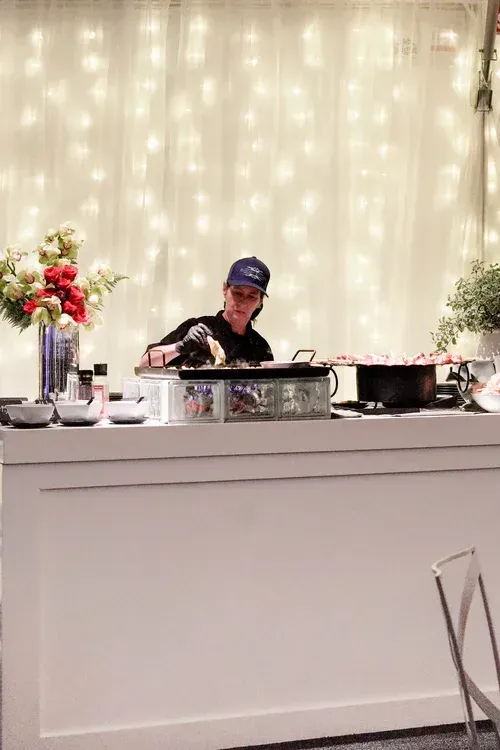 Chef cooking at a buffet station in front of a lit curtain backdrop with floral arrangements