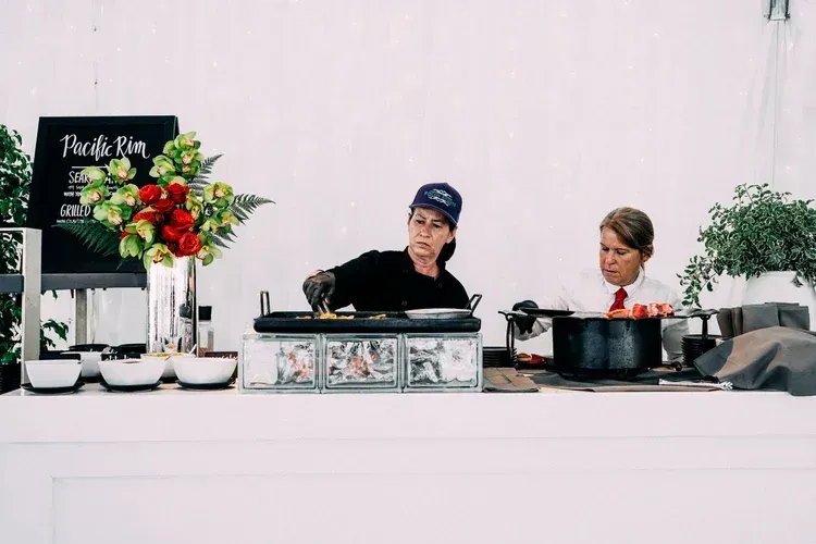 Two people preparing food at a decorated table with flowers and cookware