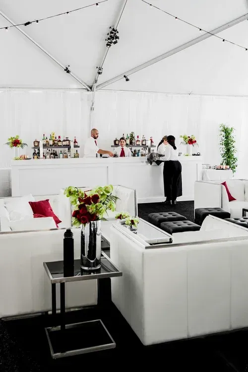 Modern white lounge tent with sofas, bar shelves, and floral arrangements
