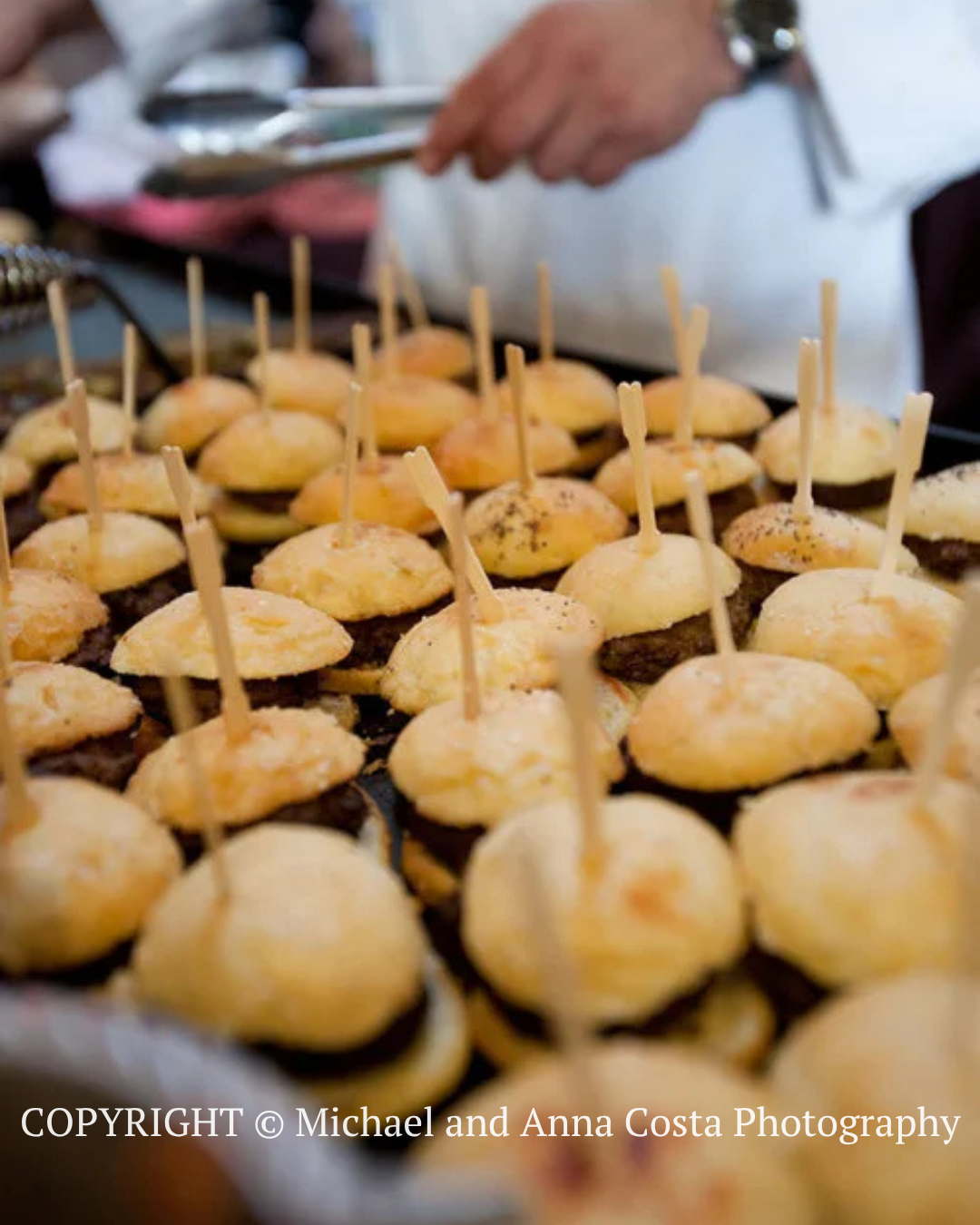 Tray of bite-size appetizers on toothpicks at a buffet, with a chef in the background