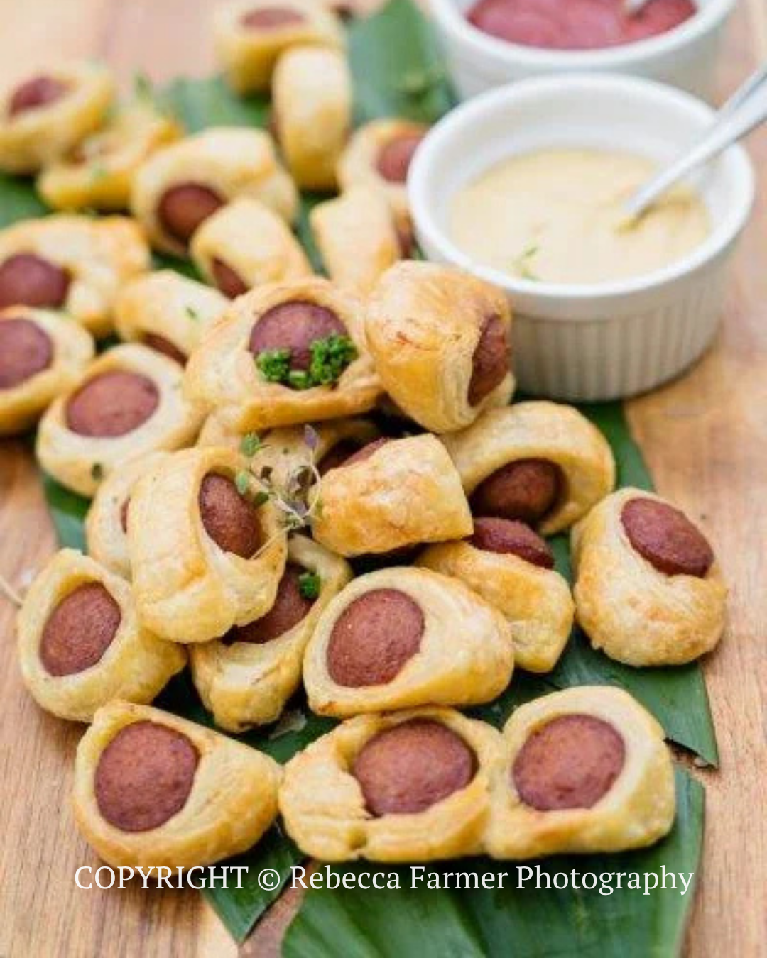 Plate of pigs in blankets with dipping sauce on a wooden board