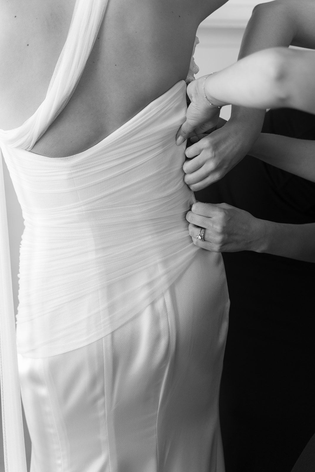 Hands adjust the back of a white dress on a person standing in a fitting room