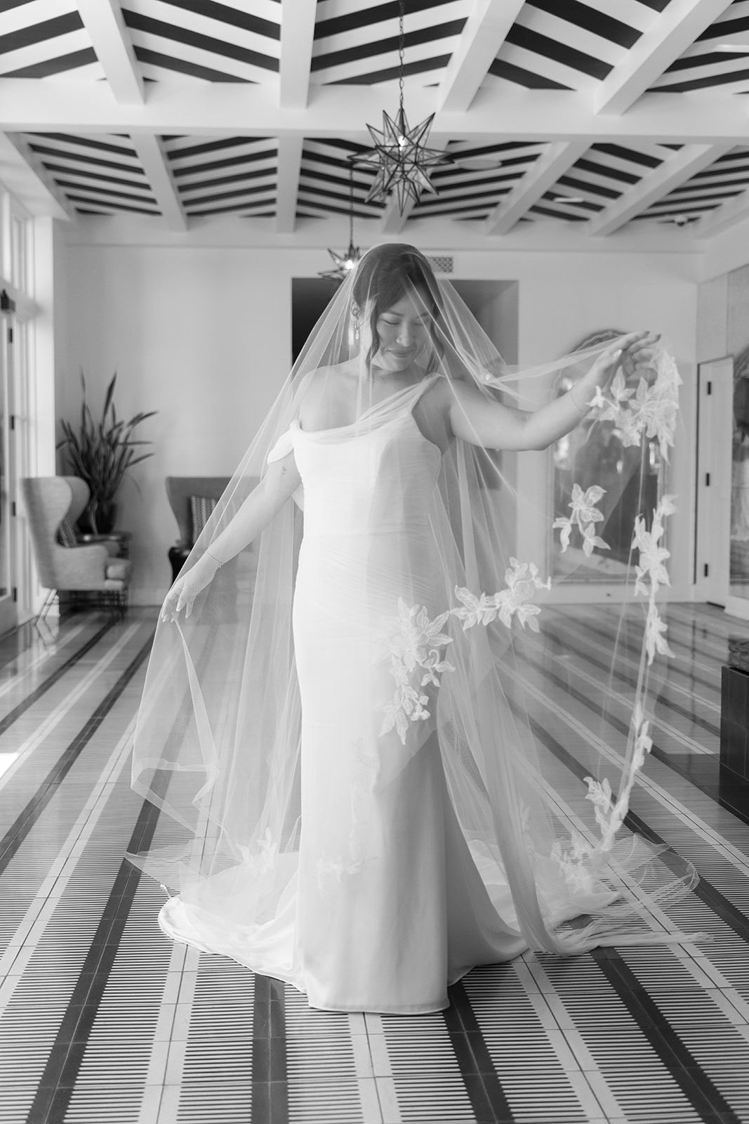 Bride in a flowing white dress and veil, standing in a decorated hallway with flowers and geometric ceiling patterns