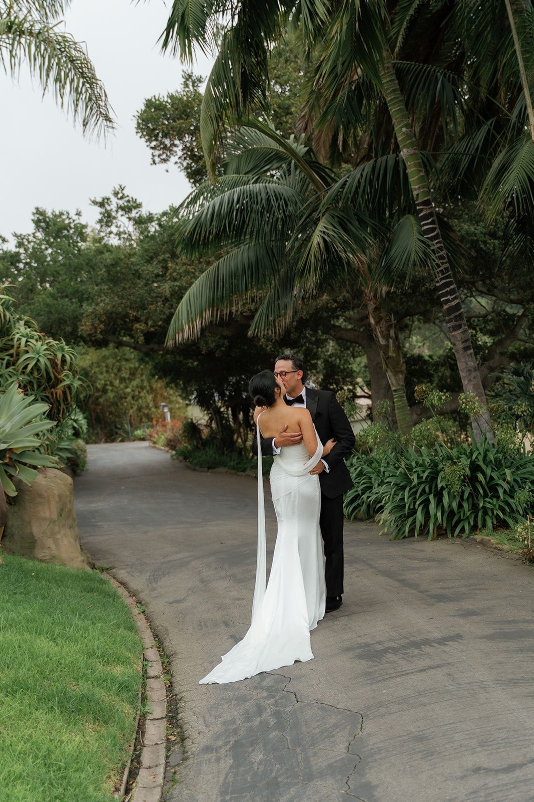 Bride and groom posing on a winding garden path surrounded by palm trees