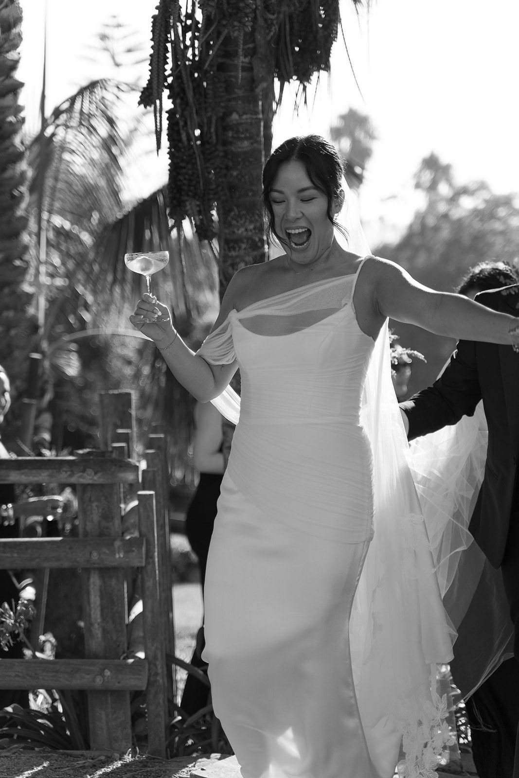 Bride in white dress holding a glass and smiling outdoors during a wedding celebration
