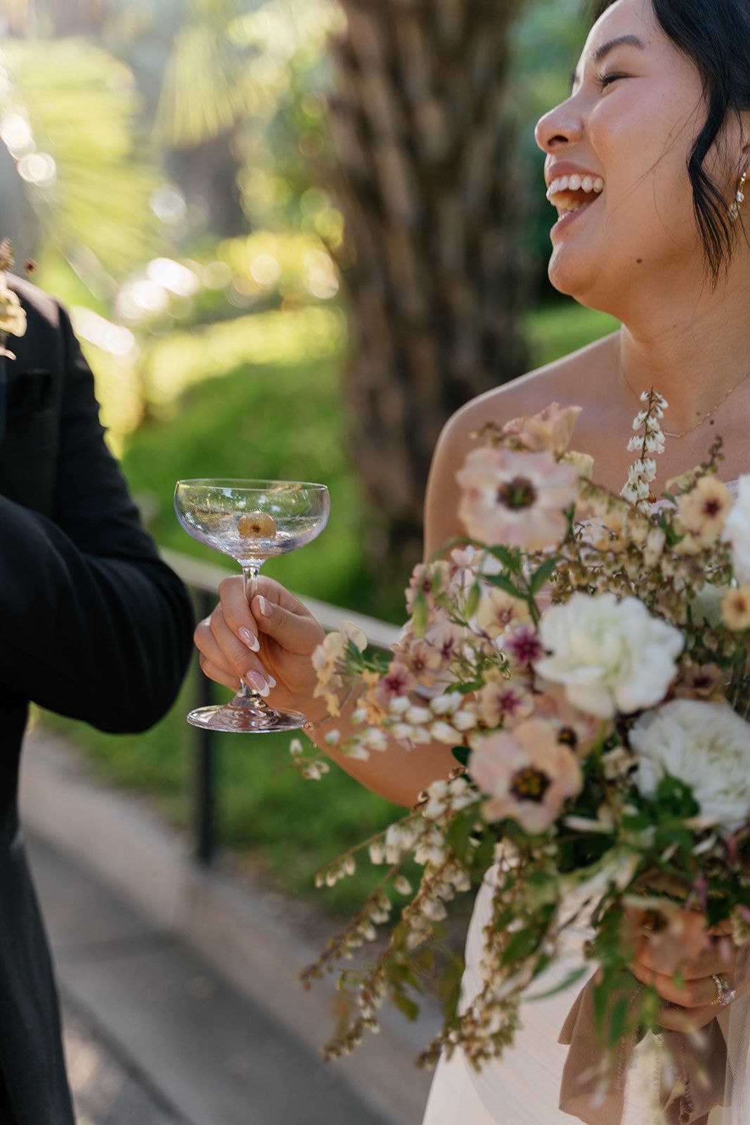 Woman in a floral dress laughing and toasting with a champagne coupe at an outdoor celebration