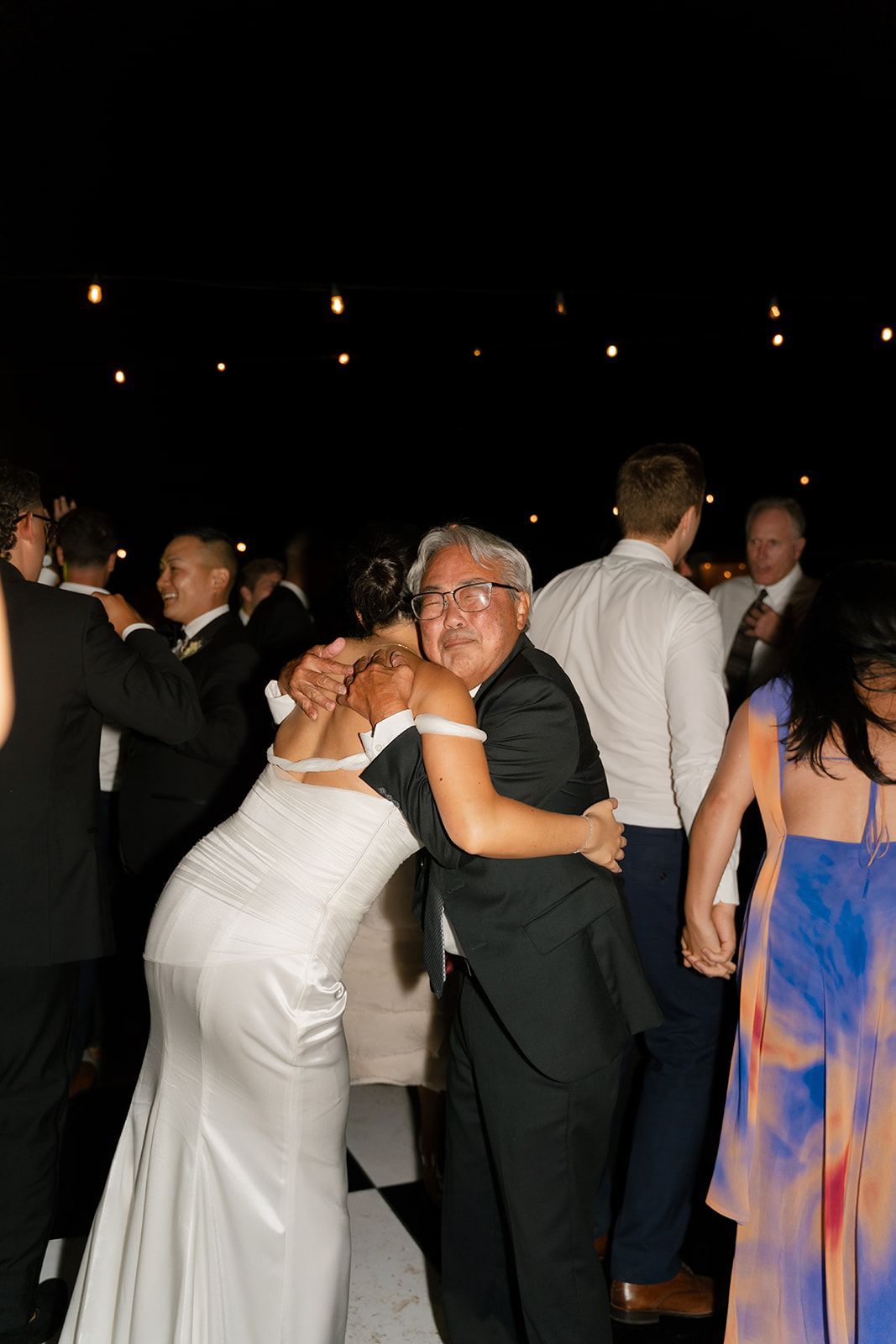 Couple dancing at a nighttime event, with guests in formal attire around them.
