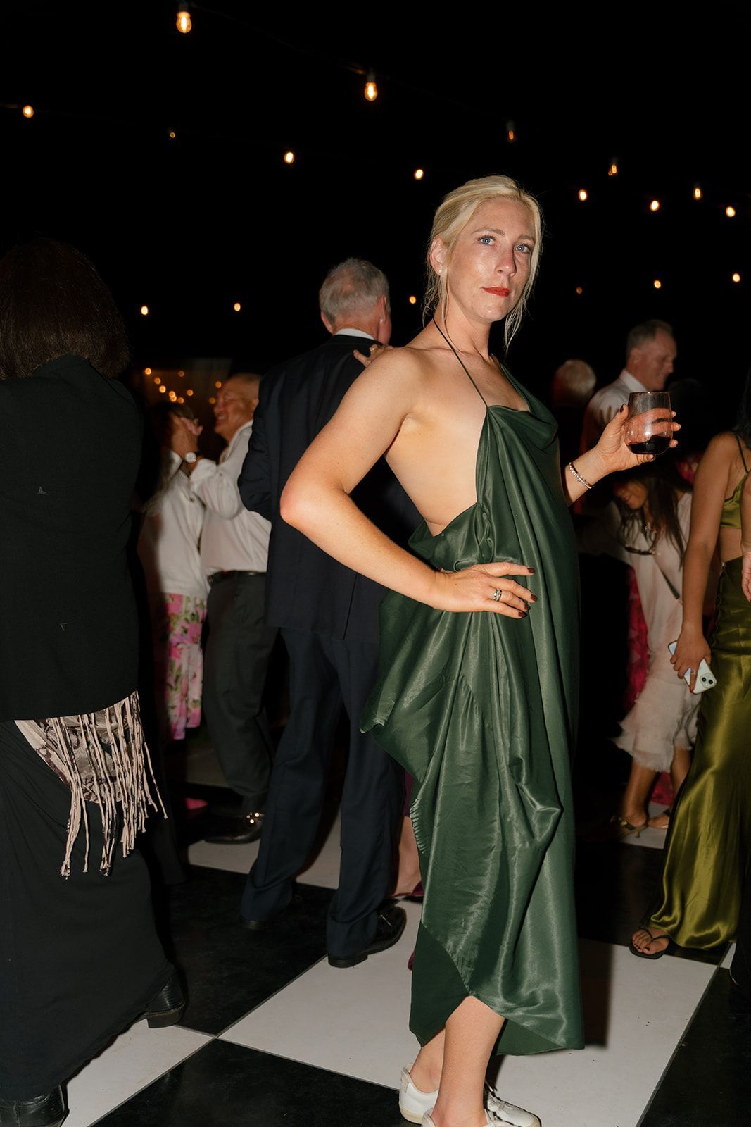 Woman in a green satin dress posing at a formal evening event with guests in the background